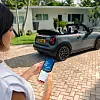 Frau schaut aufs Handy, im Hintergrund steht ein Mini Cabrio