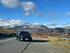 Schwarzer Mercedes-Benz CLA steht am Straßenrand in Norwegen, umgeben von Bergen mit Schneefeldern, klarer Himmel mit Wolken im Hintergrund.