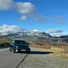 Schwarzer Mercedes-Benz CLA steht am Straßenrand in Norwegen, umgeben von Bergen mit Schneefeldern, klarer Himmel mit Wolken im Hintergrund.