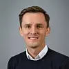 Lächelnder Mann mit kurzen braunen Haaren im dunklen Pullover vor einfarbig grauem Hintergrund, Halbportrait frontal