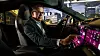 Ein Manager sitzt auf dem Fahrersitz eines Porsche und bedient den großen digitalen Touchscreen im Cockpit. Durch die Fenster ist eine nächtliche Stadtlandschaft zu sehen.