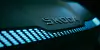 Nahaufnahme eines Skoda-Schriftzugs auf einem dunkel beleuchteten Bauteil mit blau leuchtenden, digital wirkenden Elementen.