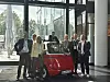 Gruppenfoto auf der CMxC 2026 Corporate Mobility Conference im Hochhaus des Süddeutschen Verlags in München mit mehreren Teilnehmenden vor einem roten Microlino-Elektrofahrzeug, Business-Konferenz zu Corporate Mobility, Elektromobilität, urbaner Mobilität, nachhaltigem Fuhrparkmanagement und neuen Fahrzeugkonzepten, Fachpublikum mit Namensschildern vor Glasfassade und moderner Veranstaltungsarchitektur, kleines Elektroauto als Symbol für flexible Mobilitätslösungen im Unternehmenskontext