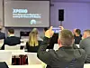 Teilnehmer der CMxC 2026 Corporate Mobility Conference fotografiert mit Smartphone einen Vortrag von XPENG im Konferenzsaal, Blick über das Publikum auf unscharfe Präsentationsfolie mit XPENG-Logo, Thema Fleet & Business, elektrische Unternehmensmobilität, internationale E-Auto-Anbieter, Elektromobilität im Fuhrpark, Business-Konferenz zu Corporate Mobility, Digitalisierung, Flottenmanagement, nachhaltiger Mobilität und neuen Fahrzeugkonzepten im Hochhaus des Süddeutschen Verlags in München