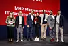 Auf einer Bühne stehen sieben Personen in Businesskleidung nebeneinander vor einer großen roten Präsentationswand. In der Mitte hält eine Person eine rote Trophäe mit der Aufschrift „IT“ in den Händen. Im Hintergrund ist der Schriftzug „MHP Management- und IT-Beratung GmbH & Co. KG“ teilweise zu sehen. Die Szene zeigt offenbar eine Preisverleihung im Rahmen einer IT- oder Automotive-Veranstaltung.