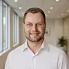 Mann mit Brille und weißem Hemd in einem hellen Büro.