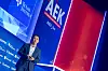 Dr. Liu Qiang, Vice President von Li Auto Inc. und General Manager des Li Auto Germany R&D Center GmbH, steht auf der Bühne des 30. AUTOMOBIL-ELEKTRONIK Kongresses 2026 in Ludwigsburg und hält einen Vortrag mit dem Titel „From Smart Vehicles to Embodied AI: Building the Silicon-Based Life Architecture of the Future“. Er trägt einen dunklen Anzug, ein helles Hemd und ein Headset-Mikrofon und hält einen Presenter in der Hand. Im Hintergrund sind das große AEK-Branding, der Hashtag #AEK_live, Sponsorenlogos wie Texas Instruments, Synopsys, Microsoft, Qualcomm und T-Systems sowie eine rot-blau ausgeleuchtete Bühnenwand zu sehen. Die Aufnahme zeigt Dr. Liu Qiang in einer nahen Bühnenperspektive während seines Vortrags über den Übergang vom Smart Vehicle zu Embodied AI, über Li Autos Technologiearchitektur, eigene Inferenzchips, 3D-Vision, große KI-Modelle, Wahrnehmung, räumliches Verständnis, autonome Fahrfunktionen, selbstständiges Laden, multimodale Interaktion, Software-Hardware-Co-Design, Fahrwerk, Bremsen, Lenkung, Aktorik, intelligente Agenten, Physical AI, chinesische Fahrzeugentwicklung, Li Auto Germany R&D Center und den AUTOMOBIL-ELEKTRONIK Kongress in Ludwigsburg.
