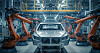 Auto in einer Fabrikmontagelinie zwischen zwei orangefarbenen Industrierobotern.