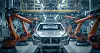 Auto in einer Fabrikmontagelinie zwischen zwei orangefarbenen Industrierobotern.