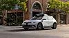Ein weißes Waymo-Robotaxi fährt durch eine Stadtstraße. Auf dem Dach sind Sensoren und ein Leuchtschild für den autonomen Fahrbetrieb zu sehen.