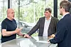 Drei Männer stehen an einem Tisch in einem modernen Büro und unterhalten sich vor großen Fenstern.