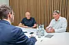 Jürgen Rittersberger sitzt mit zwei Kollegen an einem Besprechungstisch in einem Besprechungsraum mit Holzlamellenwand.