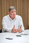 Rittersberger sitzt an einem Tisch, spricht und gestikuliert; vor ihm liegen Unterlagen und Smartphones.