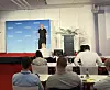 Mann auf einer Bühne vor blauem Banner in einem Konferenzraum mit sitzendem Publikum.