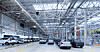 Mehrere Autos in einer hellen Fabrikhalle mit Metallkonstruktion und Produktionsanlagen.