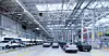 Mehrere Autos in einer hellen Fabrikhalle mit Metallkonstruktion und Produktionsanlagen.