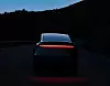 Rückansicht eines Tesla bei Nacht auf einer dunklen Straße mit leuchtender roter Rückleuchte.