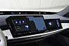 Innenraum eines BMW 7er mit großem zentralen Infotainment-Display und separatem Bildschirm auf der Beifahrerseite. Die Anzeige zeigt unter anderem Navigation, Mediensteuerung, Wetterinformationen und weitere digitale Fahrzeugfunktionen.