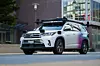 Weißer Zoox-Test-SUV fährt auf einer Straße vor einem modernen Gebäude.