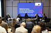 Podiumsdiskussion vor einem Bildschirm über KI und Zusammenarbeit im industriellen Umfeld, Publikum sitzt im Raum.