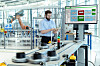 Mitarbeiter bedient ein Tablet neben einer automatisierten Produktionsanlage mit Industrieroboter und Softwareanzeige.