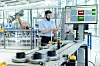 Mitarbeiter bedient ein Tablet neben einer automatisierten Produktionsanlage mit Industrieroboter und Softwareanzeige.