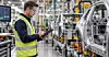 Mitarbeiter mit Tablet in einer Fabrik neben einer Montagelinie für Fahrzeugteile.