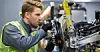 Mitarbeiter in Warnweste arbeitet an einer Maschine in einer Fabrikhalle.