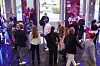 Menschen in einem hellen Eingangsbereich mit Glaswänden und leuchtenden Anzeigen.