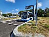 Ein weiß-blauer Shuttlebus steht auf einer Teststraße neben einem Sensorpfosten und Fahrbahnmarkierungen.