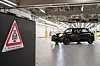 Ein schwarzer Mini fährt in einer hellen Werkhalle an einem Warnschild vorbei.
