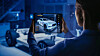 Eine Frau betrachtet auf einem Tablet ein digitales 3D-Modell eines Autos. Im Hintergrund ist ein Fahrzeugchassis in einer blau beleuchteten Entwicklungsumgebung zu sehen.
