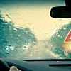 Ein Autofahrer sitzt bei schlechten Wetterverhältnissen hinteerm Steuer und sieht nur noch den Regen auf der Windschutzscheibe und ein warnendes Verkehrsschild.