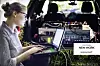 Frau sitzt am Laptop hinter einem Versuchsfahrzeug