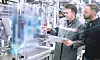 Zwei Mitarbeiter von Bosch blicken in einer Produktionshalle auf eine digitla eGrafikillustration, während einer der beiden ein Tablet in der Hand hält.