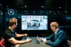 Zwei Männer sitzen an einem Tisch und betrachten ein weißes Fahrzeug von Mercedes-Benz auf einem Bildschirm. Einer der Männer bedient dabei ein Tablet.