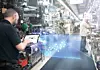 Ein Bosch-Mitarbeiter mit einem Tablet steht in einer Produktionshalle und blickt auf die Illustration einer 3D-Grafik.