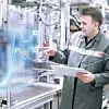 Zwei Mitarbeiter von Bosch blicken in einer Produktionshalle auf eine digitla eGrafikillustration, während einer der beiden ein Tablet in der Hand hält.