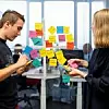 Zwei Studierende stehen vor einer Glaswand mit bunten Post-it-Zetteln