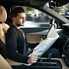 Ein Mann liest am Steuer eines autonomen Autos eine Zeitung.