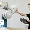 Ein Roboter von Stäubli wird von einem Mensch berührt.