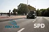 Ein autonom fahrender ID.Buzz auf einer Brücke. Im Vordergrund die Logos von CDU/CSU und der SPD.