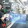 Ein Bosch-Mitarbeiter mit einem Tablet steht in einer Produktionshalle und blickt auf die Illustration einer 3D-Grafik.