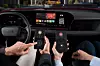 Zwei Personen sitzen in einem Audi-Fahrzeug und bedienen über ihre Smartphones das In-Car-Gaming-System AirConsole. Auf dem zentralen Infotainmentdisplay ist das Spiel „UNO Car Party!“ sichtbar. Die Smartphones zeigen virtuelle Gamecontroller mit Bedienfeldern an. Das Fahrzeug befindet sich im Stand. Das Audi-Logo ist am Lenkrad erkennbar, der Innenraum modern und digital gestaltet.
